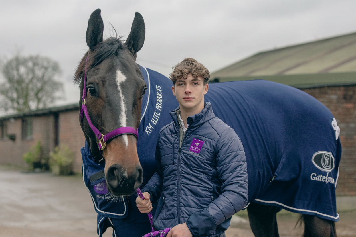 Man standing next to a horse wearing a blue rug with visible KM Elite branding.